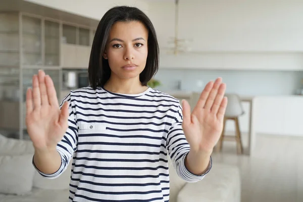 stock image Young woman showing stop gesture by palms, warning sign of prohibition or rejection, looking at camera at home. Serious strict female protesting against domestic violence, abuse, gender discrimination