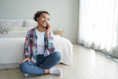 Sabah telefon görüşmesi. Genç Afrikalı Amerikalı kadın yatak odasında akıllı telefondan arkadaşıyla konuşuyor. Günlük giysili tatlı İspanyol genç kız telefon bağımlısı. İletişim ve rahatlama.