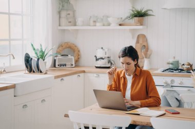 Bayan satış müdürü, evden çalışıyor. Turuncu gömlekli genç İspanyol kadın uzaktan çalışıyor. Bayan Freelancer dizüstü bilgisayar kullanarak not alıyor ve internette geziniyor..