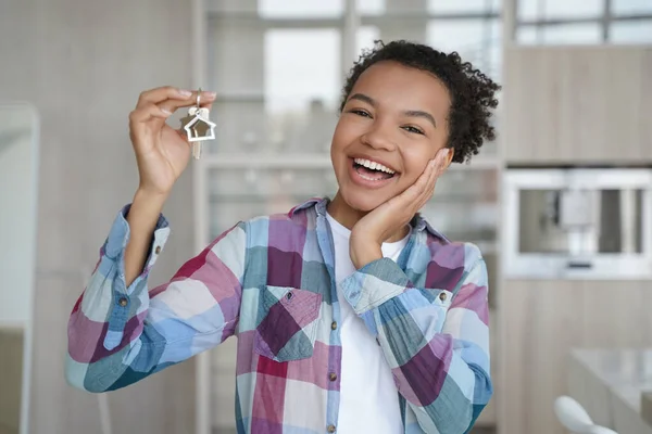Overjoyed young african american lady is holding key from new apartment. Happy teenage girl rents her first home. Mortgage loan, real estate purchase and relocation conceptual image.