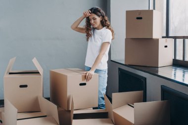 Karton kutuları açan kafası karışık bir kadın. Yeni dairede yorgun bir kız. Bayan alnına eliyle dokunur, yorgun kişinin jesti. Paketleme, nakliye ve taşınma konsepti.