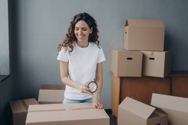 Young woman is packing boxes with duct tape. Lady is wrapping cardboard containers with tape. Moving service worker preparing boxes for shipping. Courier is packing things for and storage.