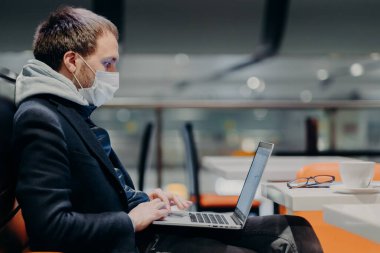Laptop bilgisayarında serbest çalışan klavyelerin yan görüntüsü, uzaktan çalışıyor, virüs salgını yüzünden karantina sırasında koruyucu maske takıyor, kahve dükkanında poz veriyor, bulaşıcı hastalıklar uyarısında bulunuyor