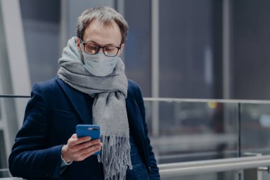 Adamın fotoğrafı telefonundan haberleri izliyor, koruyucu maske takıyor, hava kirlenmesinden ya da koronavirüsten koruyor, e-posta kutusunu kontrol ediyor, sıcak atkı takıyor. Covid-19. Salgın hastalık. Sağlık, sosyal medya