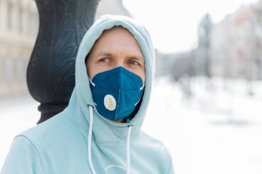 Ciddi düşünceli adam sokakta yürürken kapüşonlu ve koruyucu solunum maskesi takıyor grip virüsü veya koronavirüsten korunuyor kalabalık yerlerden kaçıyor, sağlığa önem veriyor.