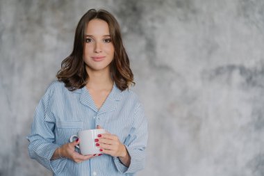 Çekici kadın kıyafeti içinde giyinmiş, beyaz kupa kahve veya çay ile tutar, sabah içsin, reklam veya promosyon içeriği kopyalama yeri olan arka plan bulanık karşı kapalı pozlar