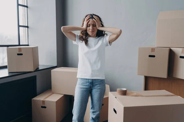 stock image Headache from moving. Exhausted woman is tired from packing cardboard boxes with duct tape. European young lady in jeans and white t-shirt going to relocate. Anxiety and stress from moving concept.