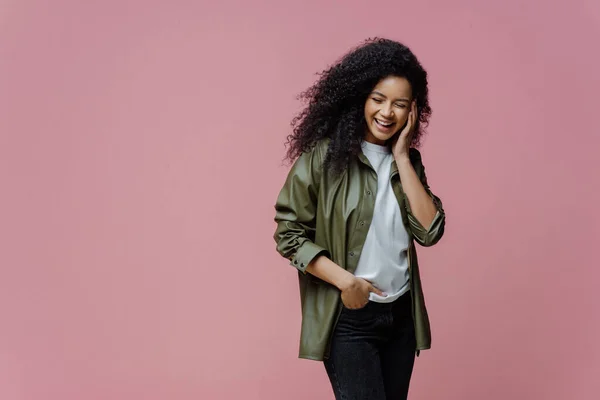 stock image Horizontal shot of happy African American woman keeps hand in pocket, laughs as hears funny anecdote, spends free time in merry company, concentrated down, isolated on pink background, copy space