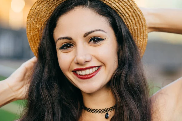 Close up portrait of cute female with dark hair, charming eyes and pleasant smile wearing straw summer hat having good mood feeling relaxation. Attractive female model with beautiful appearance