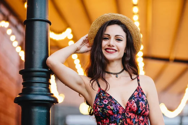 Fashionable elegant woman wearing dress with flower print and straw hat, posing at camera with smile, feeling relaxation, having good mood. People, beauty, lifestyle, facial expression, youth concept