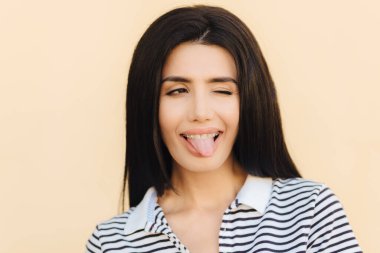 Komik neşeli esmer erkek dil, göz ile yanıp söner gösterir yapar yüz buruşturma, diş teli takıyor, uzun düz siyah lüks saçlı kayıtsızca, ışık arka plan üzerinde izole giyinmiş. İnsanlar ve mutluluk