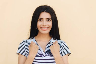 Neşeli hoş gülümseme ile kadın, yumruk, giyer parantez dişlerde, elinde tutar vardır izole bej renkli arka plan üzerinde siyah düz saçlı. Genç kafkas kadın umut daha iyi, jestleri için heyecanlı