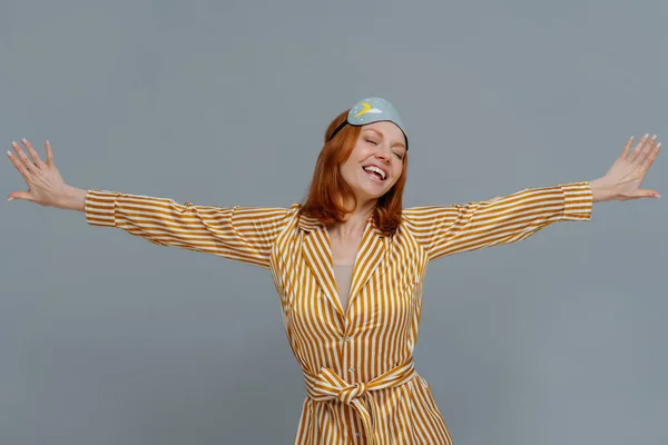 Positive Relaxed Woman Wears Blindfold Striped Robe Stretches Arms Sideways — Stock Photo, Image