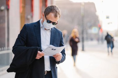 Coronavirus hastalığı. Ciddi bir erkek bankacı gazete okur, dünyadaki salgın hastalıkları öğrenir, koruyucu maske takar, virüsün yayılmasını önler, sokakta durur..