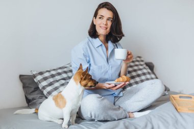 Rüya gibi esmer kadın oturuyor geçti bacaklar rahat yatak yatak, düşünceli bir yana, görünüyor portresi jack tutar fincan kahve ve kruvasan ve onun favorisi Rusya korkunç