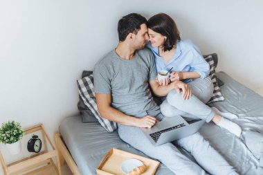 Güzel romantik çift öpecek, birbirlerini yatağa, filmleri izlemek için kullanma dizüstü bilgisayar otururken bakmak, kahve içmek, beraberlik ve dinlenme odasında keyfini çıkarın. İlişki kavramı