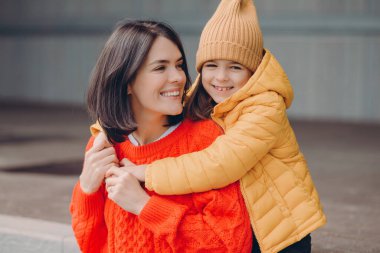 Memnun genç annenin fotoğrafı kızına olumlu bakıyor, anneyi kucaklıyor, birliktelikten zevk alıyor, dişlek gülümsemeler, mutluluk dolu gözler, iyi ilişkiler. Aile fotoğrafı.