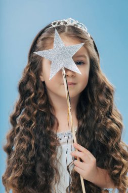 İyi görünümlü küçük kadın çocuğun uzun kıvırcık saçlı, giyer taç, Kapalı atış kapsar şeklinde yıldız, sihirli değnek ile yüz açık mavi renkli izole. Çocuk ve büyü kavramı