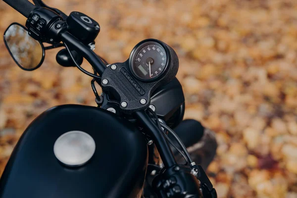 stock image Close up shot of black motorbike against ground covered with orange foliage in autumn park. Transportation, riding and traveling concept.