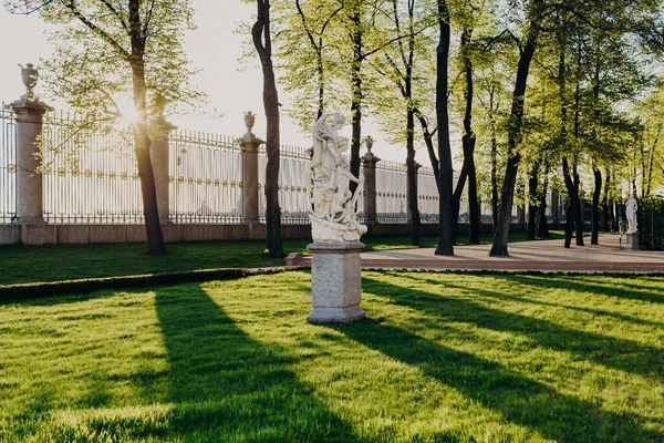 Outdoor shot of Summer Garden in Saint Petersburg. Peace and Victory sculpture. Beautiful view with green lawn, sunshine and grille in background. Places of entertainment in Russia