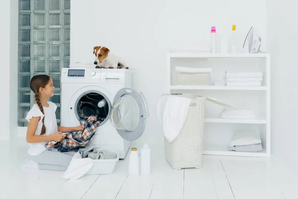Menina Positiva Esvaziando Máquina Lavar Roupa Mantém Camisa Xadrez Limpo — Fotografia de Stock