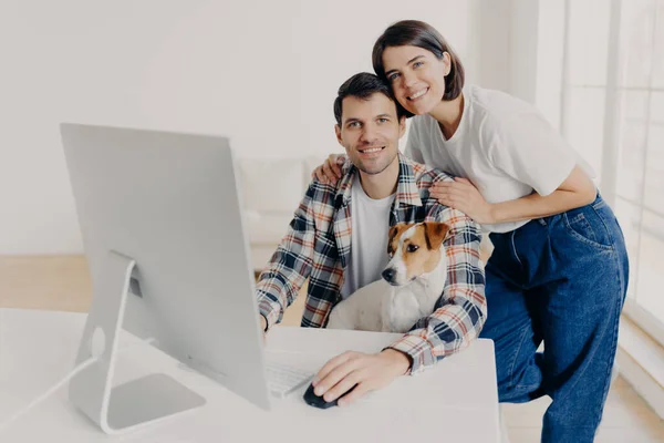 快乐的家庭夫妇在电脑前摆姿势 远程合作 有自己的生意 在网上赚钱 高兴地看着相机 和心爱的宠物玩耍 — 图库照片