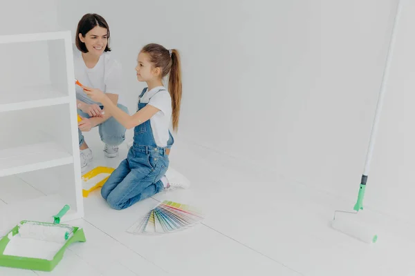 소녀와 어머니는 서랍을 흰색으로칠 페인트 솔이나 롤러스케이트를 사용하며 견본으로 둘러싸인 — 스톡 사진