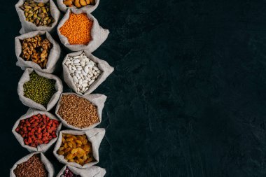 Reklam Için kopya alanı ile siyah arka plan üzerinde izole fasulye tohumu ve kurutulmuş meyve ile dolu küçük çuvallar üst görünümü