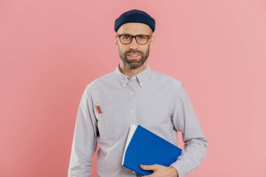 Görüntü kendini genç erkek ile anız, şeffaf gözlük takar, ders kitabı kol altında tutar, proje çalışması hazırlar, pembe bir arka plan karşı modelleri emin. Not defteri pozlar kapalı ile işadamı.