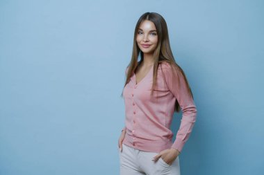 Güzellik ve moda konsepti. Genç ve çekici bir kadın, kendine güvenen, tasasız, şık giyinen, saçları önemseyen, mavi arka planda kalan, başarılı bir alışveriş gününden sonra mutlu olan bir kadın.