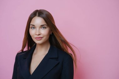 İşe giden muhteşem kadın yöneticinin portresi, siyah resmi kıyafet, doğal makyaj, kameraya özgüven, pembe stüdyo arka planına karşı duruyor. İnsanlar ve bakım konsepti.