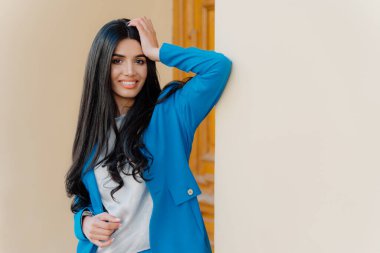 Gülümseyen esmer genç kadının yatay çekim baş bir elini tutar, resmi giyim giymiş, dişgülümseme, uzun düz siyah saçlı, kamera mutlu görünüyor. İş kadını toplantıya geliyor