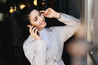 Beyaz önlük karanlık kaşları, gözler, saf deri, kafasını bir kenara gülümseyen seyir el cep telefonu dokunmadan üzerinden sohbet güzel manikür sahip zarif esmer ince kadın at kuyruğu ile giyinmiş