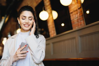 Yüksek sesle müzik onun kulaklık tadını çıkarırken gözleri sevinçle kapanış güzel görünümü ile dinlendirici esmer kadın. Şık kadın serbest zaman ve gevşeme yaparken onun favori müzik dinlemek