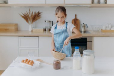 Önlüklü küçük tatlı bir kız, malzemeleri çırpıcıyla karıştırır, yumurta, süt, un kullanır, yeni tarifler dener, mutfağın içinde durur, lezzetli kurabiyeler veya fırın hazırlar, nasıl pişirileceğini öğrenir..