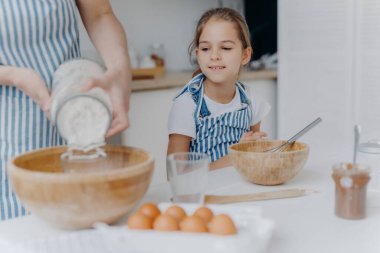 Meraklı küçük kız annesinin hamur işini nasıl hazırladığını, yemek yapmayı öğrendiğini, mutfak tecrübesi kazandığını, önlük giydiğini görüyor. Yüzü olmayan kadın kaseye un ekler, diğer malzemelerle birlikte, mutfakta çocukla poz verir.