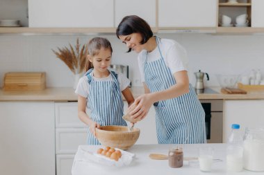 Kız ve anne yemek yapmayı, çizgili önlük giymeyi, lezzetli bir yemek hazırlamayı, farklı malzemeler kullanmayı, mutfak rutinini, evde durmayı severler. Çocuklar, annelik, aşçılık kavramı..