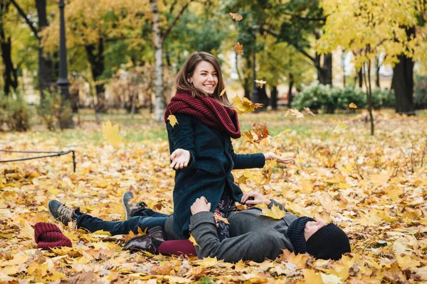 긍정적 여성은 스카프를 두르고 나뭇잎을 하늘에 던지고 가을철을 즐기는 것처럼 — 스톡 사진