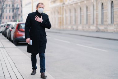 Adamın açık hava çekimi işe gidiyor, nefes almakta zorlanıyor, elini göğsünde tutuyor, tıbbi maske takıyor, salgın hastalıklarla ilgileniyor, dışarıda poz veriyor. Virüs saldırısı, sağlık sorunu kavramı