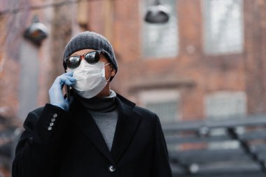 Hasta adam virüs salgını sırasında koruyucu maske takıyor, arkadaşıyla telefonda konuşuyor, siyah ceket ve güneş gözlüğü takıyor, dışarıda poz veriyor. Sağlığınızı koruyun. Coronavirus, panik konsepti