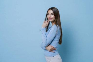 Güzel Avrupalı genç bir kadının profil çekiminde ince yapılı, mavi kazak ve beyaz pantolon giymiş, fotoğraf çekiminde modeller, bakımlı bir yüzü, sağlıklı bir teni var, makyaj yapıyor..