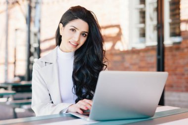 Teknoloji ve iletişim kavramı. Güzel görünümlü bir kafe ifade kamera açık otururken seyir gülümseyen sahip dizüstü bilgisayar üzerinde çalışan başarılı Avrupa iş kadını