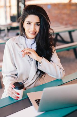 Doğrudan kameraya bakarak ücretsiz kablosuz bağlantı kullanarak elektronik cihaz ve laptop, e-posta kontrol kahve ile kafe istirahat zevk genç esmer kadın girişimci dikey portresi