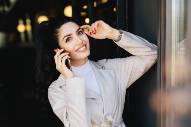 Bu güzel hanımla koyu saç ve gözler, kalıcı makyaj ve geniş baş taraftan holding kocasıyla smartphone üzerinde konuşurken gülümseyen dudak yatay portresi. Şık giysileriyle güzel kadın