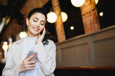 At kuyruğu bağlı koyu saçlı güzel kadın portresi resmen gözleri cep telefonu tutan gevşeme ile kapanış kulaklık ile müzik giyinmiş. İnsanlar, yaşam tarzı, teknoloji