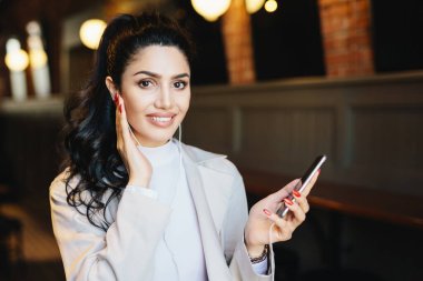 Cep telefonu online müzik app kullanarak genç iş kadını rahat kafe kulaklık, favori parça dinlerken poz resmi beyaz elbise giyen güzel görünümü ile portresi