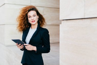 Onun iş ortağı yakın kafe, bekleyen elinde, tablet tutan zarif elbiseler giymiş güzel işkadını kıvırcık kabarık saçlı ücretsiz internet conncection kullanarak. İnsanlar, kariyer, iş