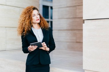 Onun çalışma günü planlama kadın girişimci kıvırcık gür saçlı resmi elbise giyiyor, modern tablet holding, dalgın bir ifadeyle bir yana, arıyorum. Dokunmatik yüzey kullanarak proje geliştirme kadın