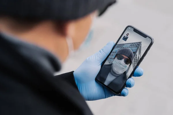 stock image Male holds phone in medical gloves, talks with friend via online conference, greets friend, discuss latest news about coronavirus in their country. Medicine, health care and video consultation