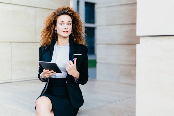 stock image Horizontal portrait of pretty confident businesswoman dressed formally, holding her pocket book with pen and tablet computer, being busy with her work. People, lifestyle, career, business concept